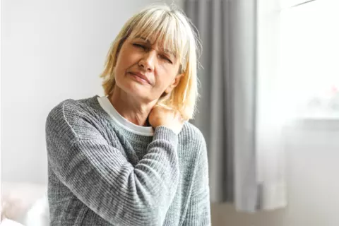 Frau hat schmerzen und fasst sich an den Nacken