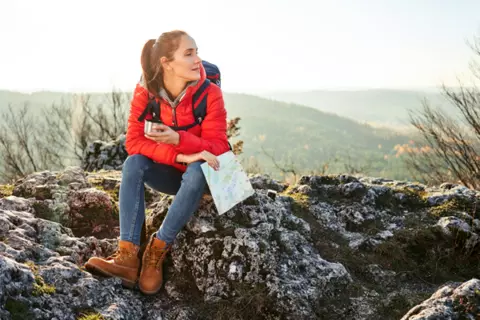 Frau macht beim Wandern eine Pause auf einem Felsen