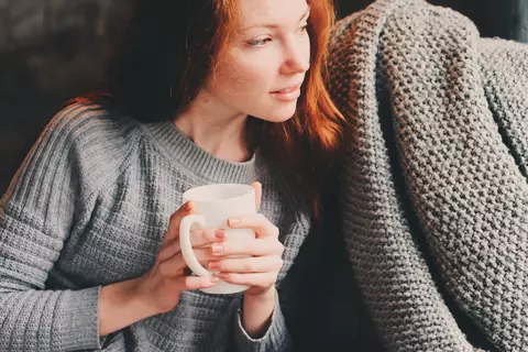 Junge Frau sitzt mit einer Tasse am Fenster