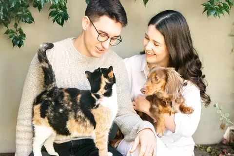 Frau und Mann sitzen mit Hund und Katze auf dem Schoß auf einer Bank