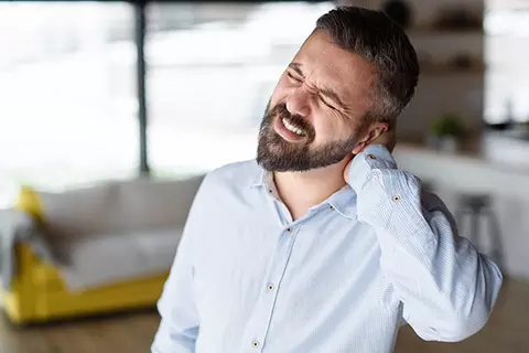 Mann hat Schmerzen und langt sich in den Nacken
