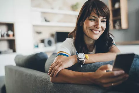 Frau sitzt auf der Couch und schaut ins Handy