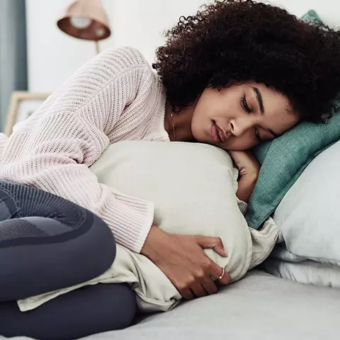 Frau liegt mit Menstruationsschmerzen im Bett