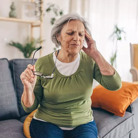 Ältere Dame ist schwindlig und setzt sich auf die Couch